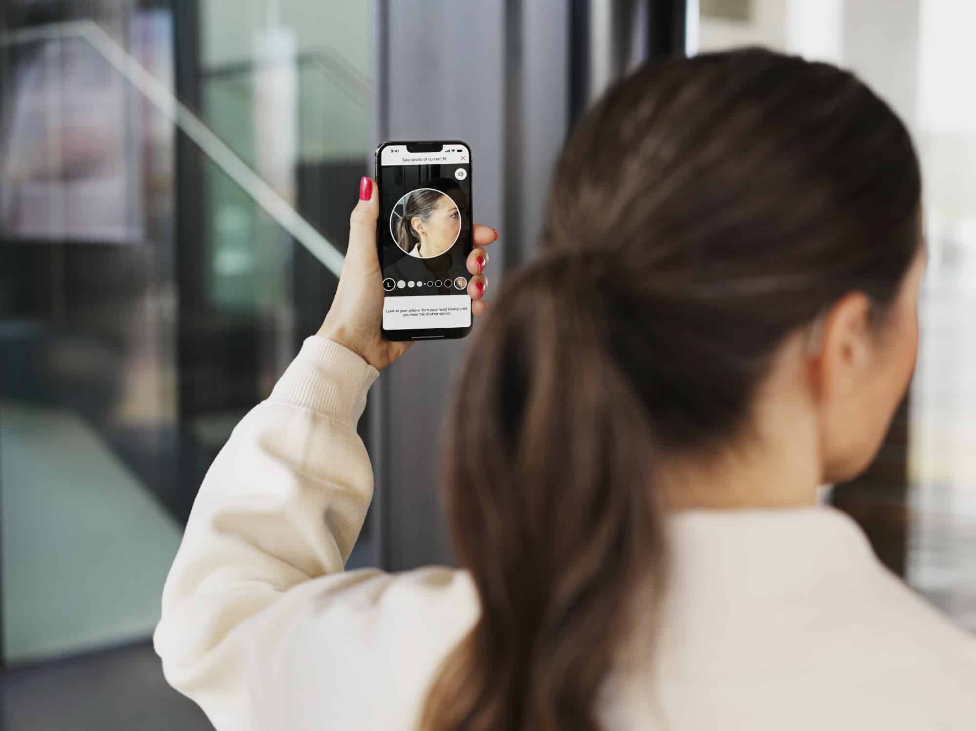 A woman checks the fit of her hearing aid using her cell phone