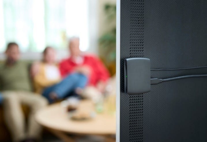 a family watches tv while an auracast streamer is connected to the back of their television