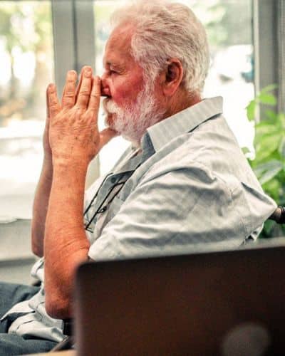 old man sitting sadly in front of a window