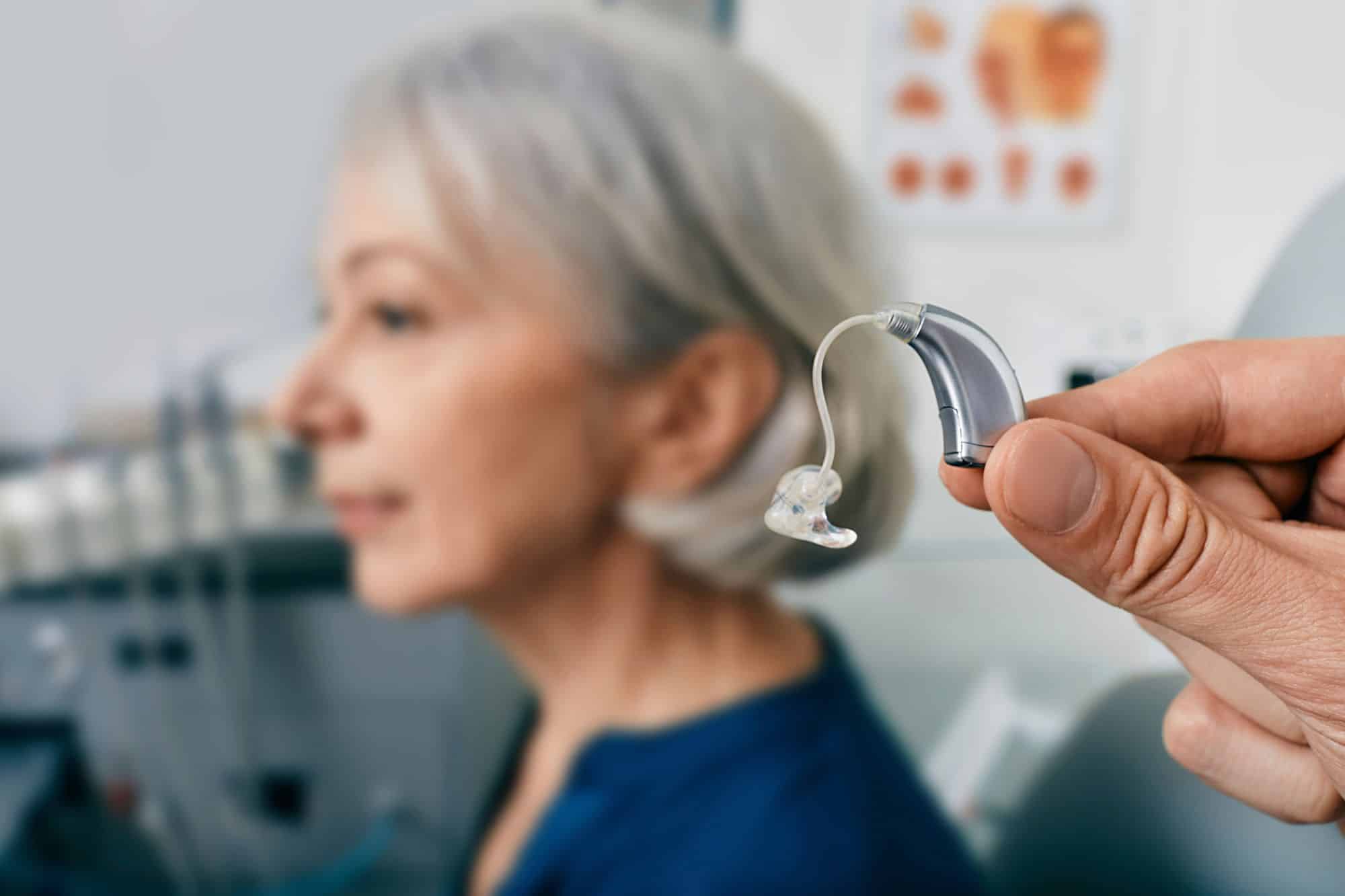 closeup of a hearing aid with a woman out of focus in the background