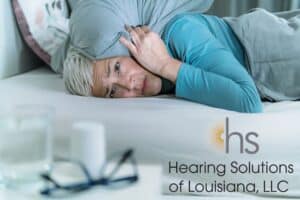 woman laying in bed holding her ears in pain